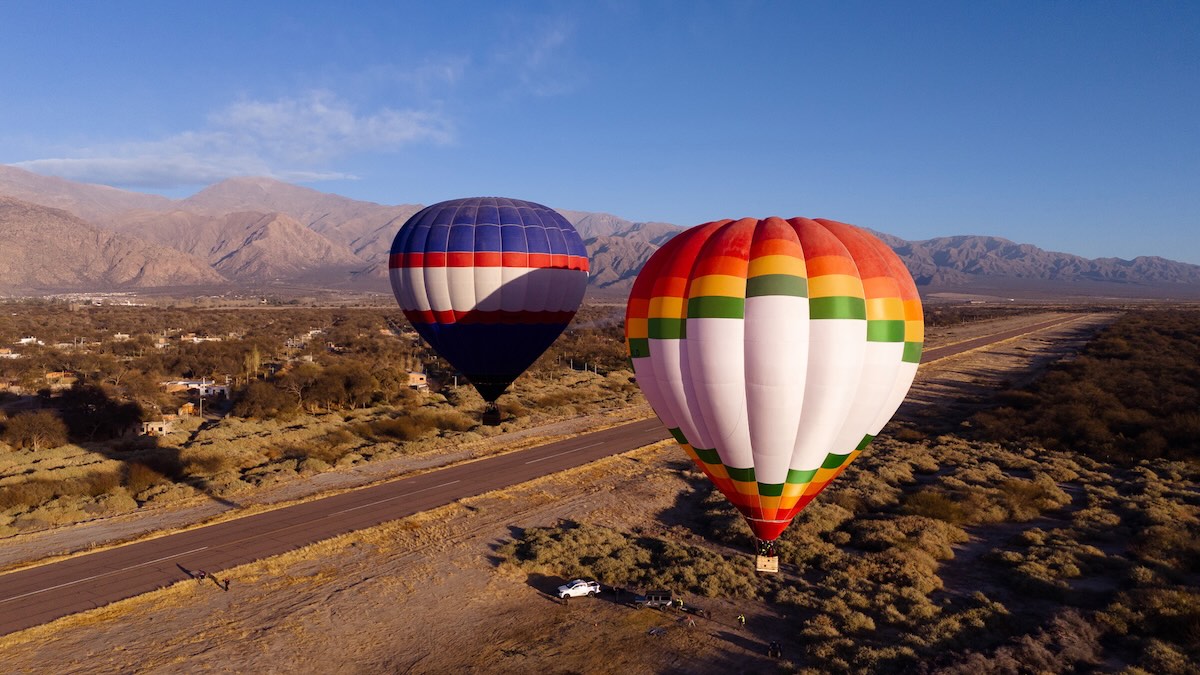 Hot air balloons soaring above the vineyards and desert landscape of Cafayate, Salta, with the Andes Mountains in the background — a luxury wine tour experience in Northern Argentina.
